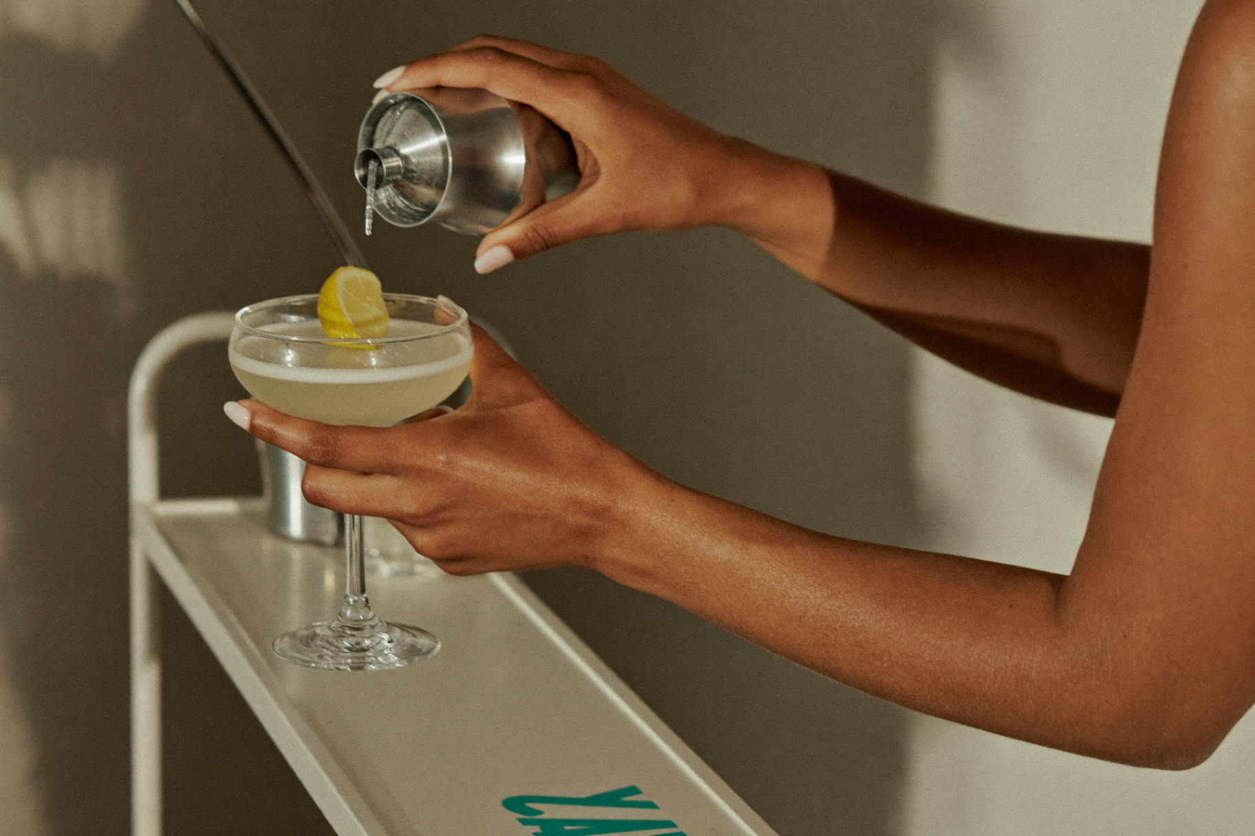 Bartender pouring a cocktail from a shaker into a coupe glass on a mobile bar cart